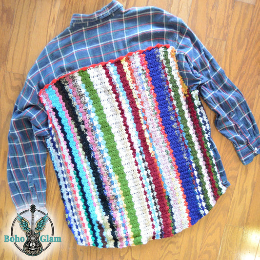 Flat Lay Back: A dark navy and green plaid flannel shirt laid flat on a wood floor, featuring a large back panel made of colorful, vertical crochet stripes in shades of blue, green, red, and white.