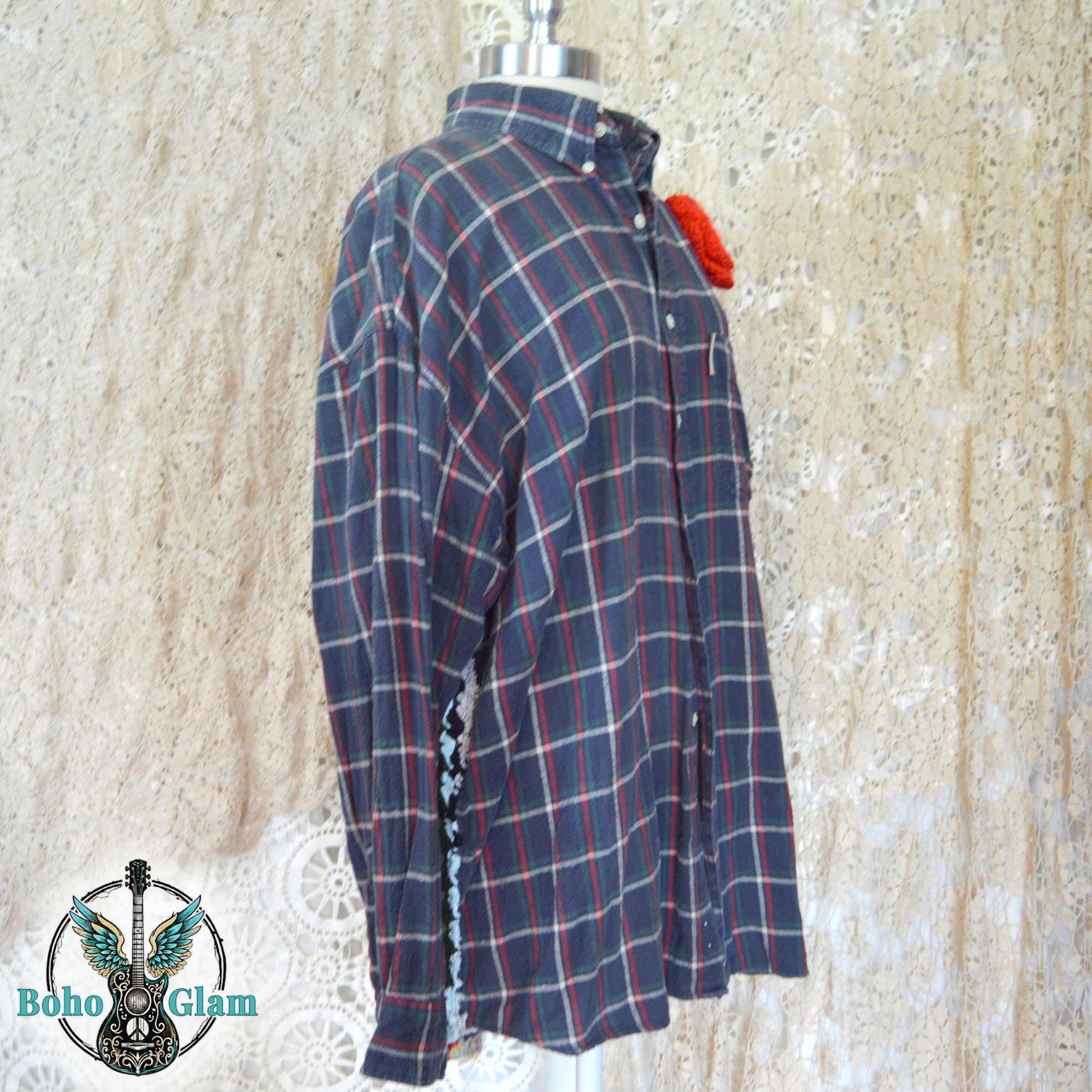 Front Angle View: A three-quarter view of the shirt on a mannequin, showing the button-front design and the red crochet floral embellishment against the dark plaid fabric.