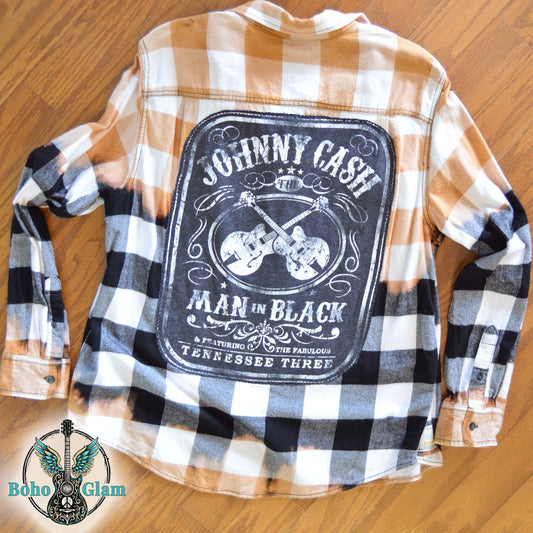 Flat Lay Back: A tan, black, and white buffalo plaid flannel shirt featuring a large back patch with Johnny Cash "Man in Black" text and crossed guitars.