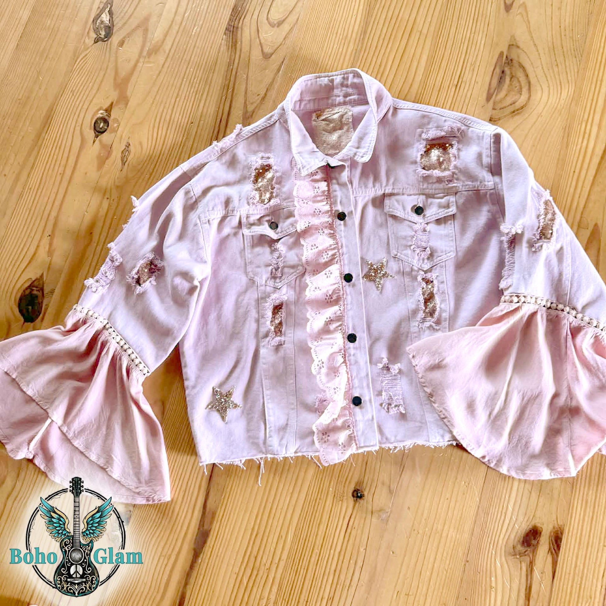Flat lay of pink cropped denim jacket with ruffle front detail, rhinestone stars and sequin patches, Stevie Nicks inspired upcycled boho jacket with dramatic sleeves