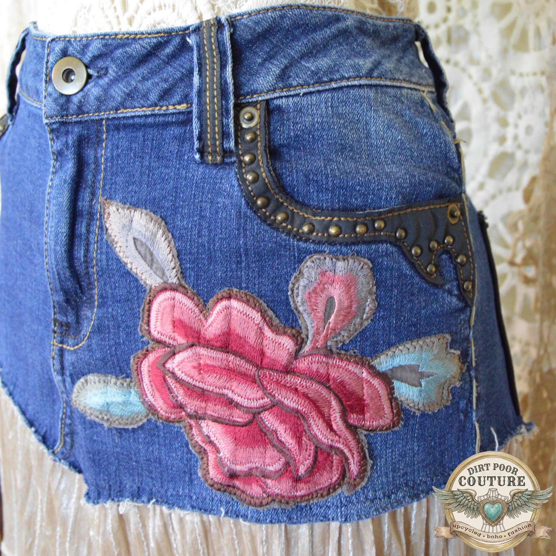 A detailed shot of the intricate red and pink peony embroidered applique below the studded denim pocket