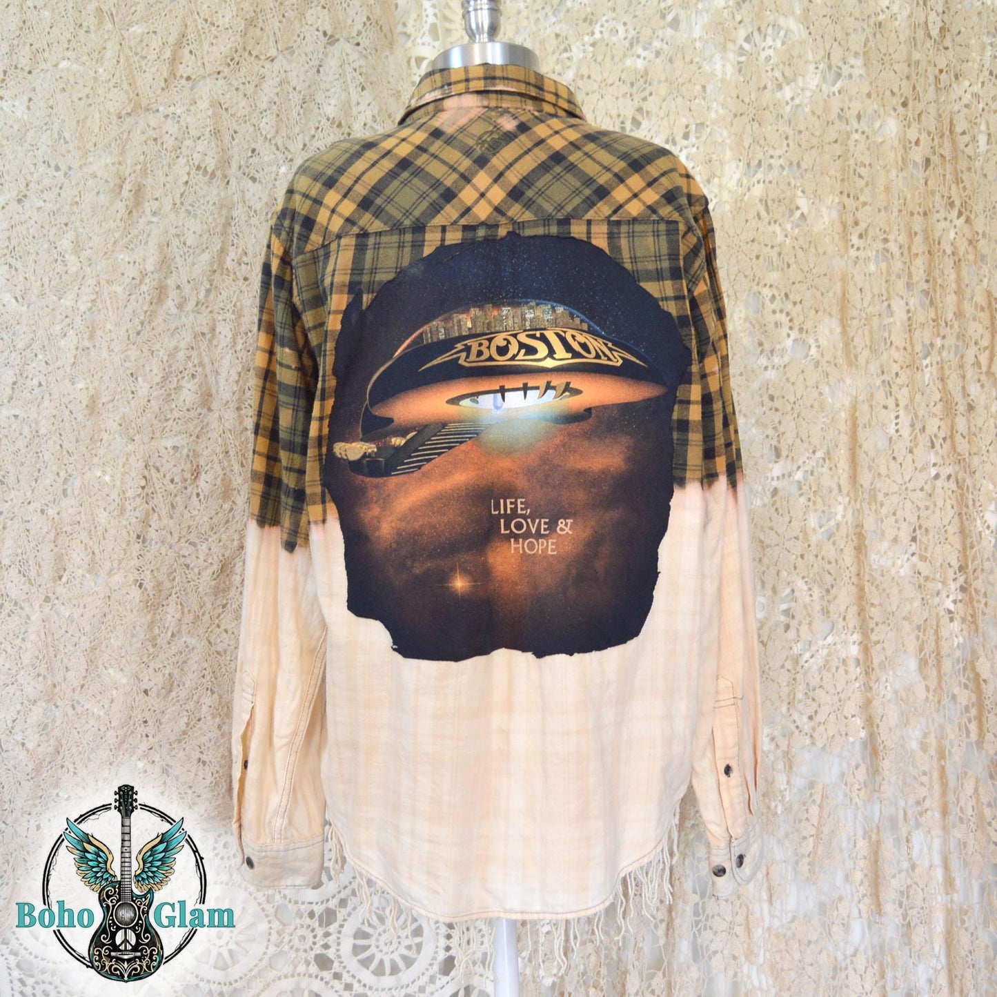 Back View: A yellow and black plaid flannel shirt with a bleached white bottom half and a large circular Boston band graphic appliqued on the back