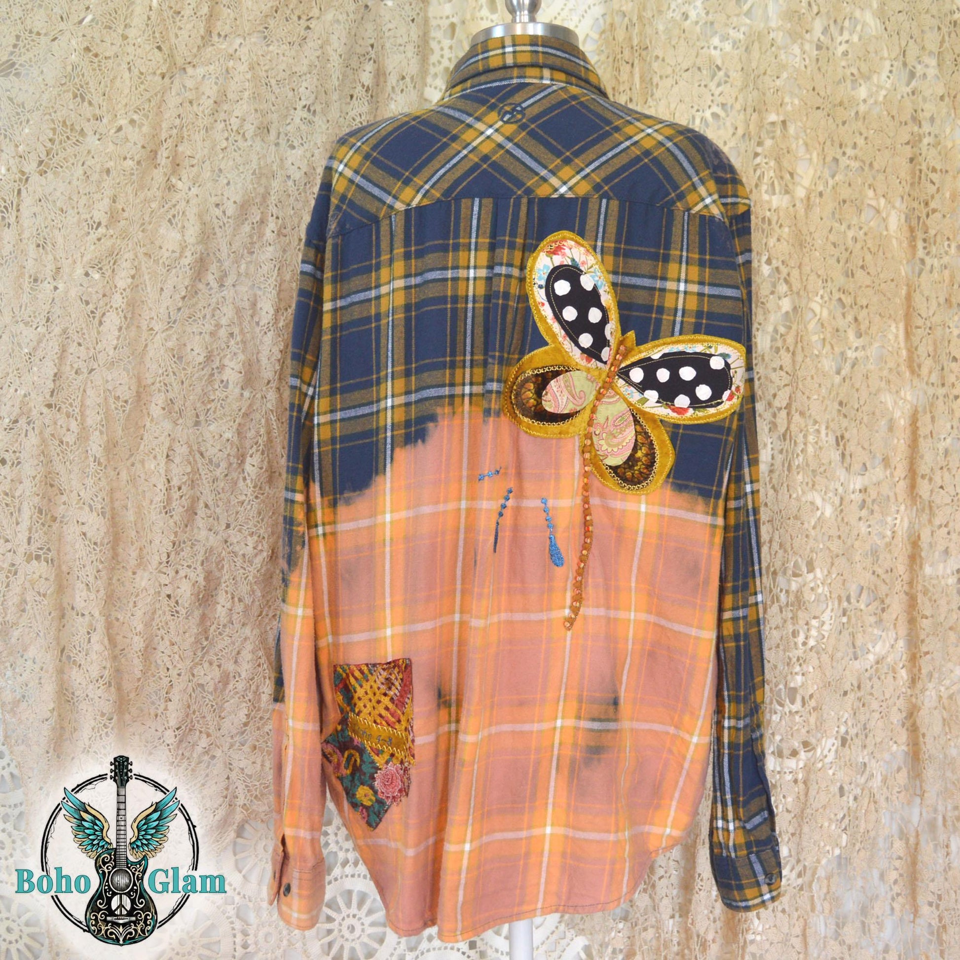 Back View: A navy and gold plaid flannel shirt with a bleached peach bottom half featuring a large butterfly applique and a 1 John 4:8 bible verse patch.