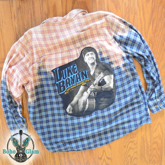 Flat Lay Back: The upcycled flannel shirt laid flat on a wood floor featuring a large Luke Bryan graphic applique across the bleached and blue plaid transition.