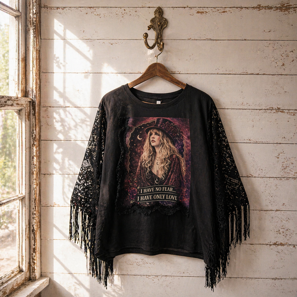 Black fringe top with graphic design hanging on a wooden hook against a rustic wooden wall.
